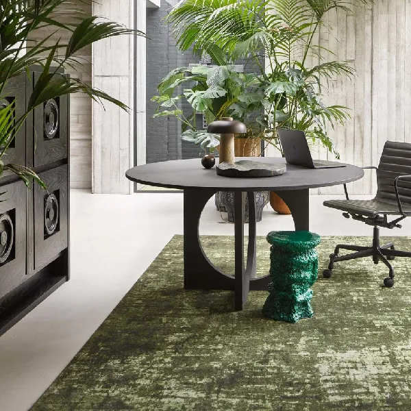 Distressed moss-green area rug under a round black table.